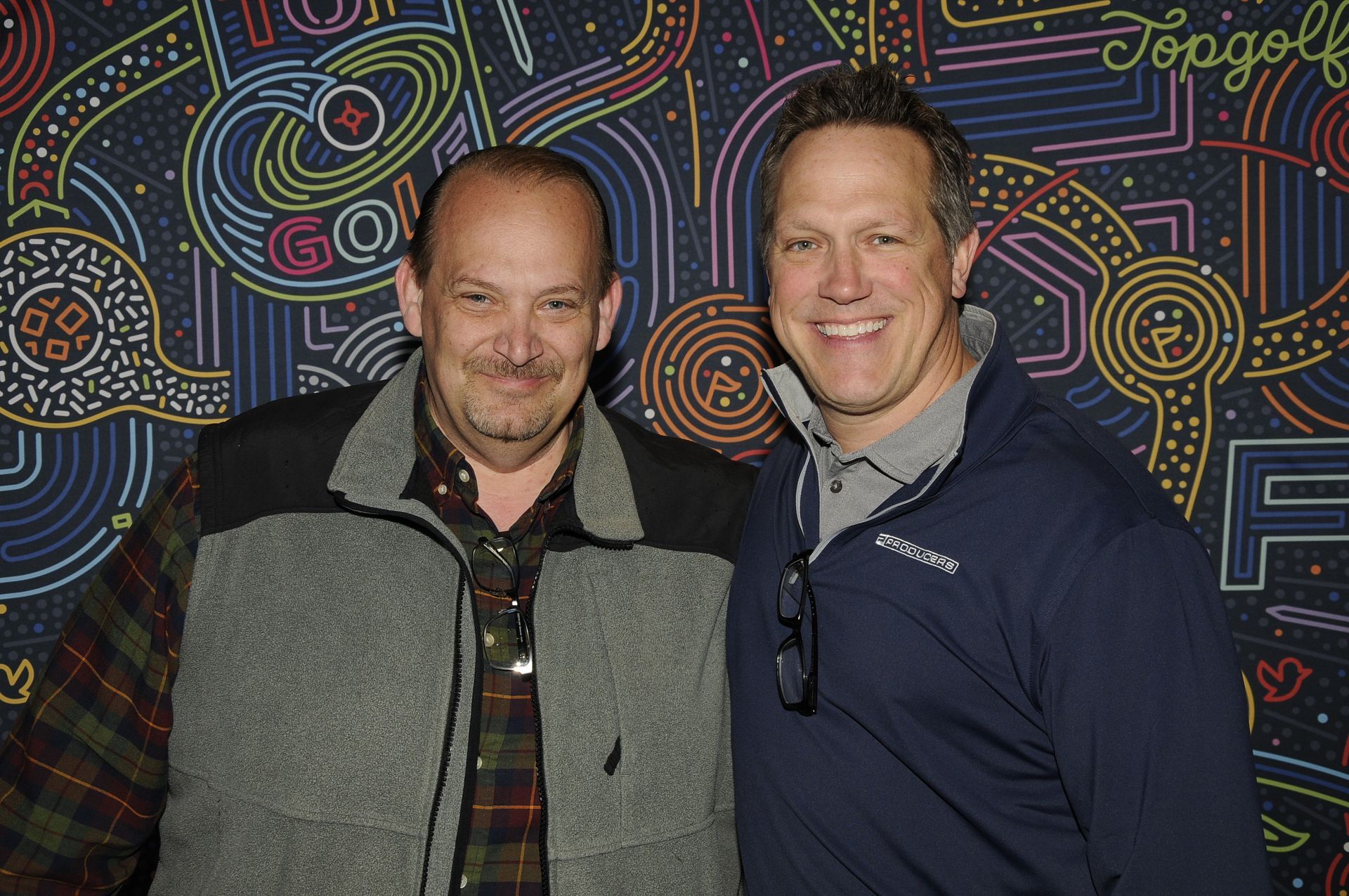 Two men are posing for a picture in front of a colorful wall.