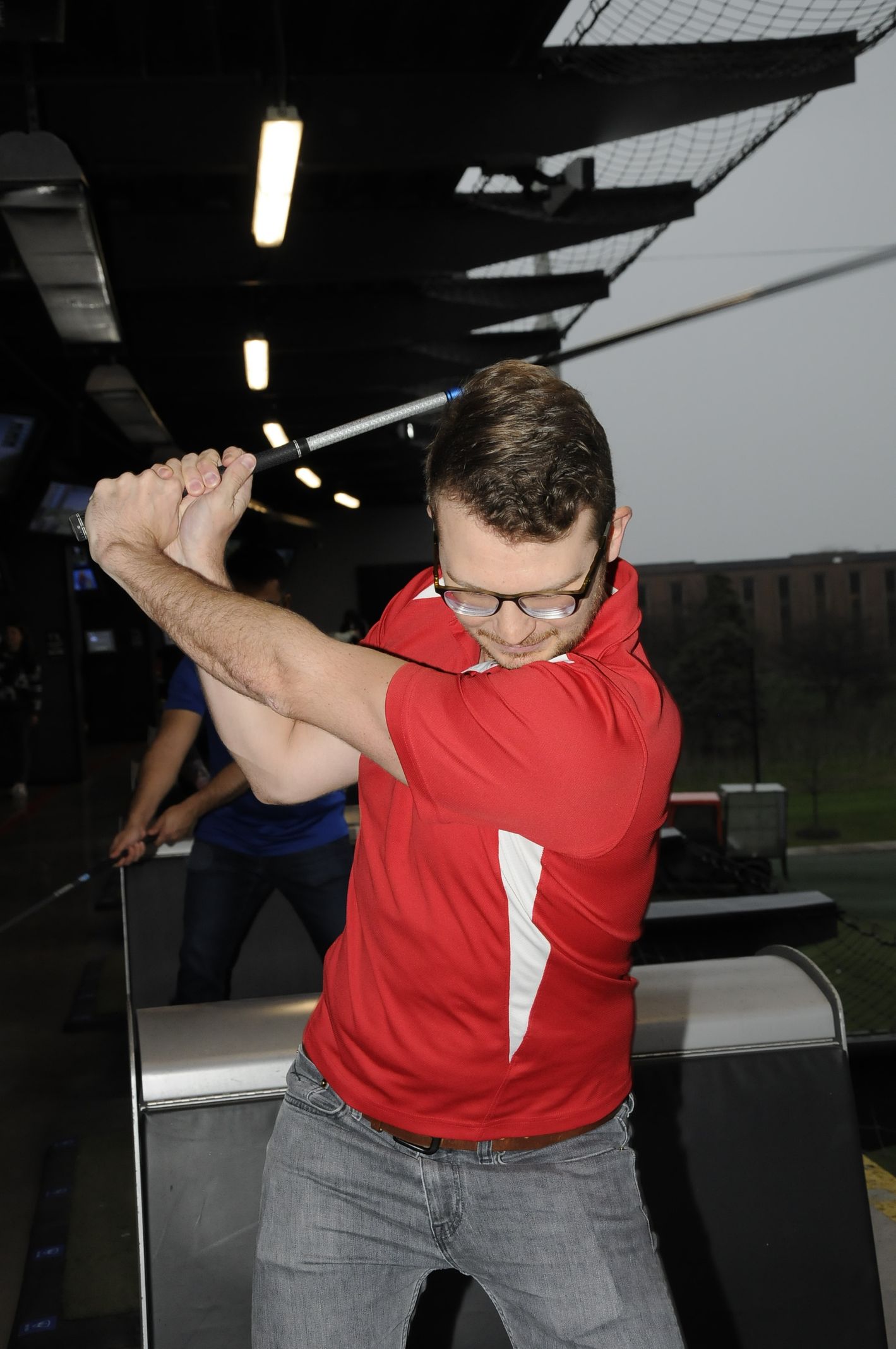 A man in a red shirt is swinging a golf club