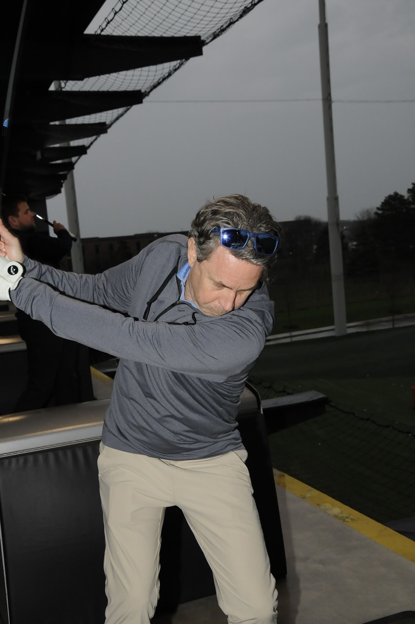 A man wearing sunglasses is swinging a golf club