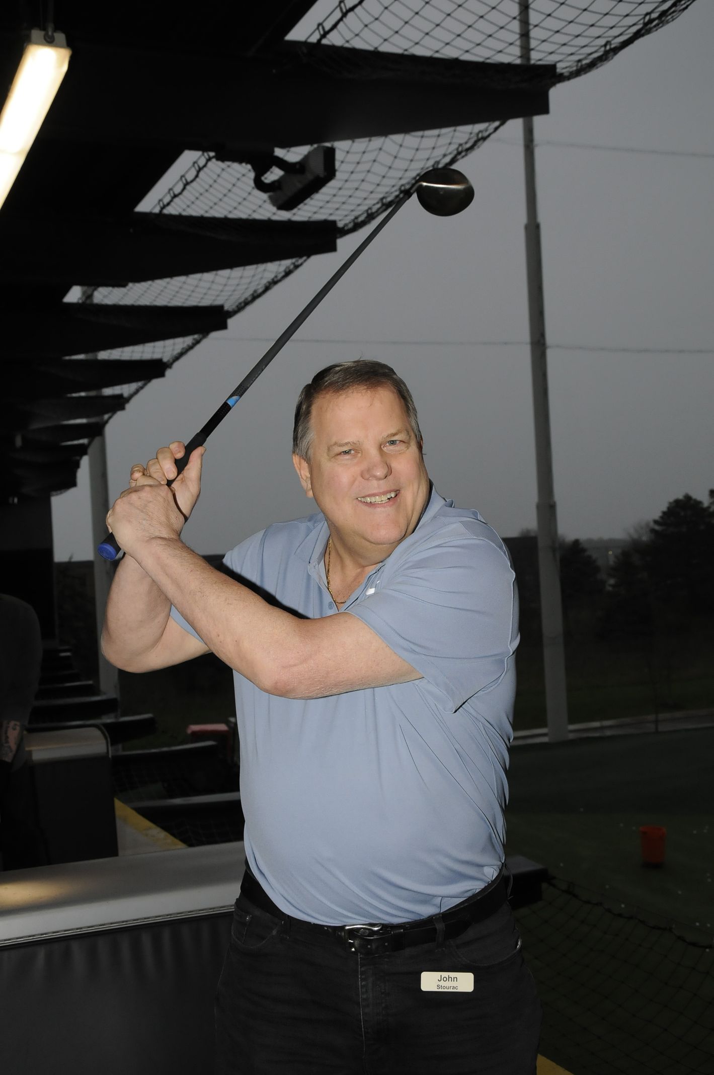 A man in a blue shirt is swinging a golf club
