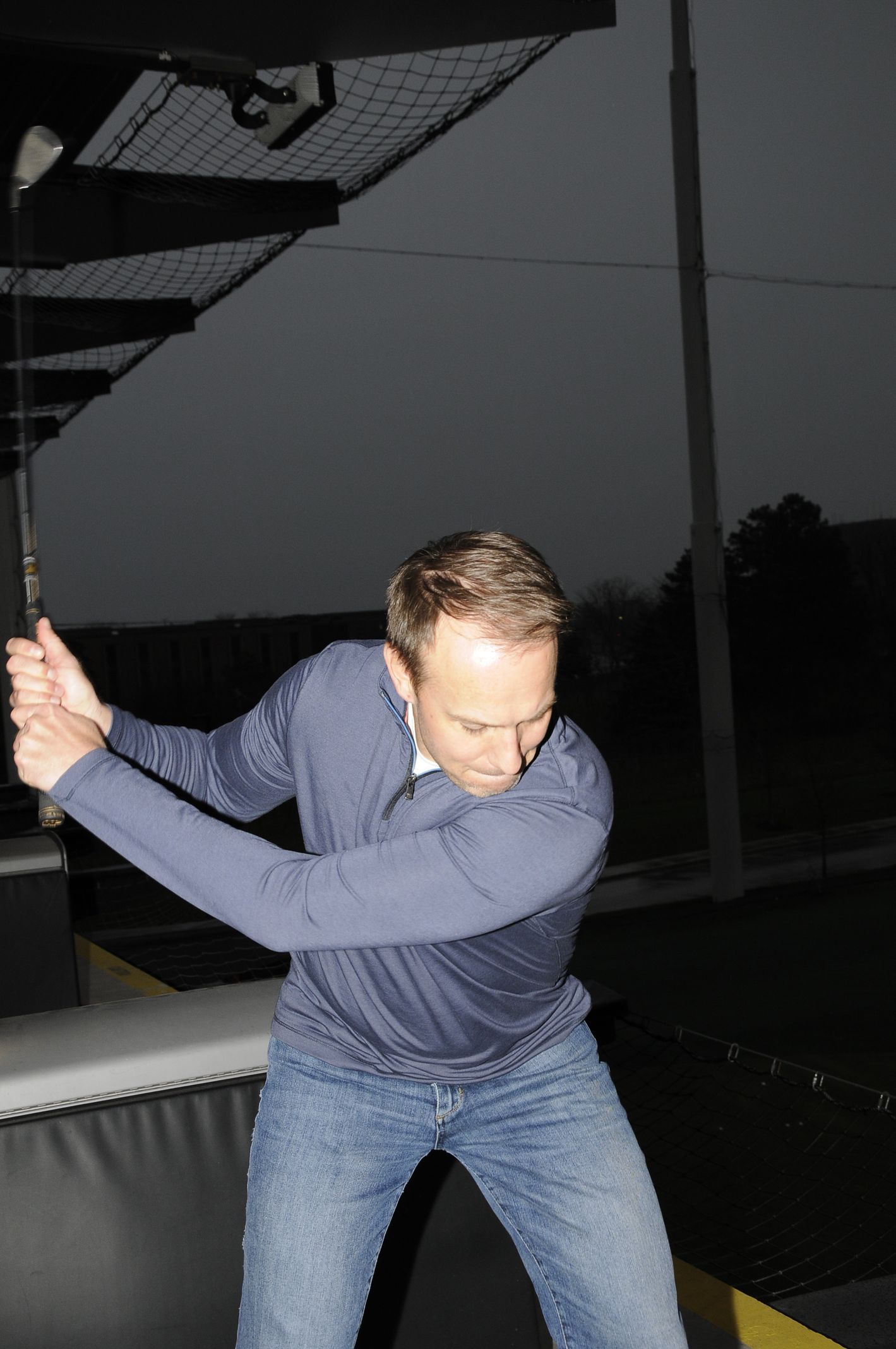 A man in a blue shirt is swinging a golf club
