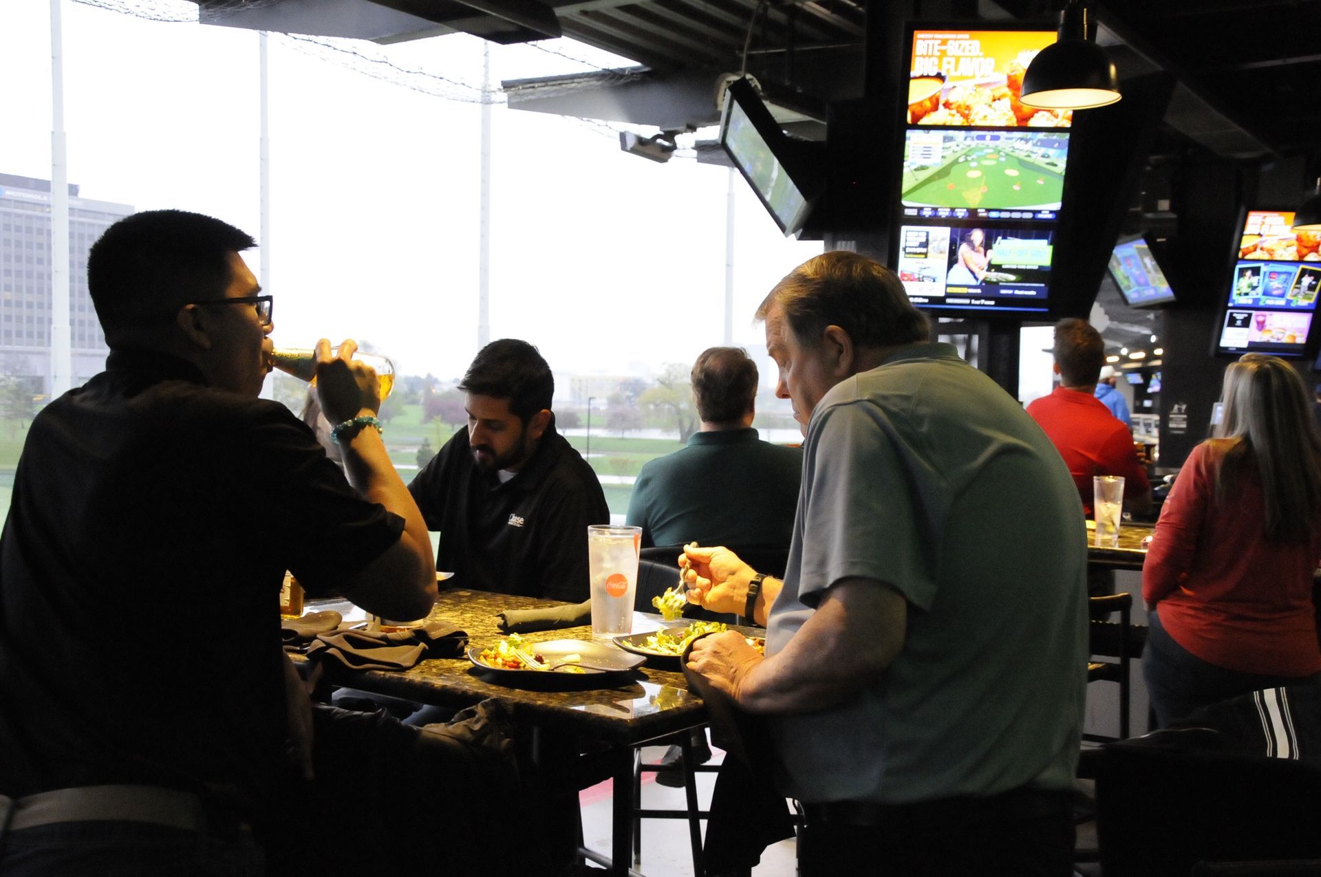 A group of people are sitting at tables in a restaurant watching sports