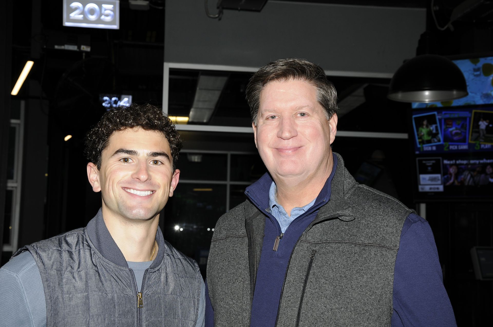 Two men are posing for a picture in front of a sign that says 205