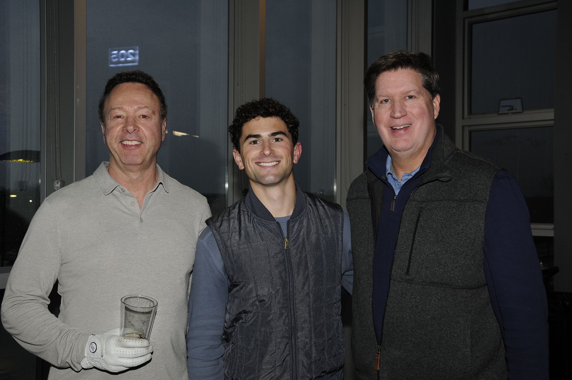 Three men are posing for a picture together and one of them is holding a glass of water.