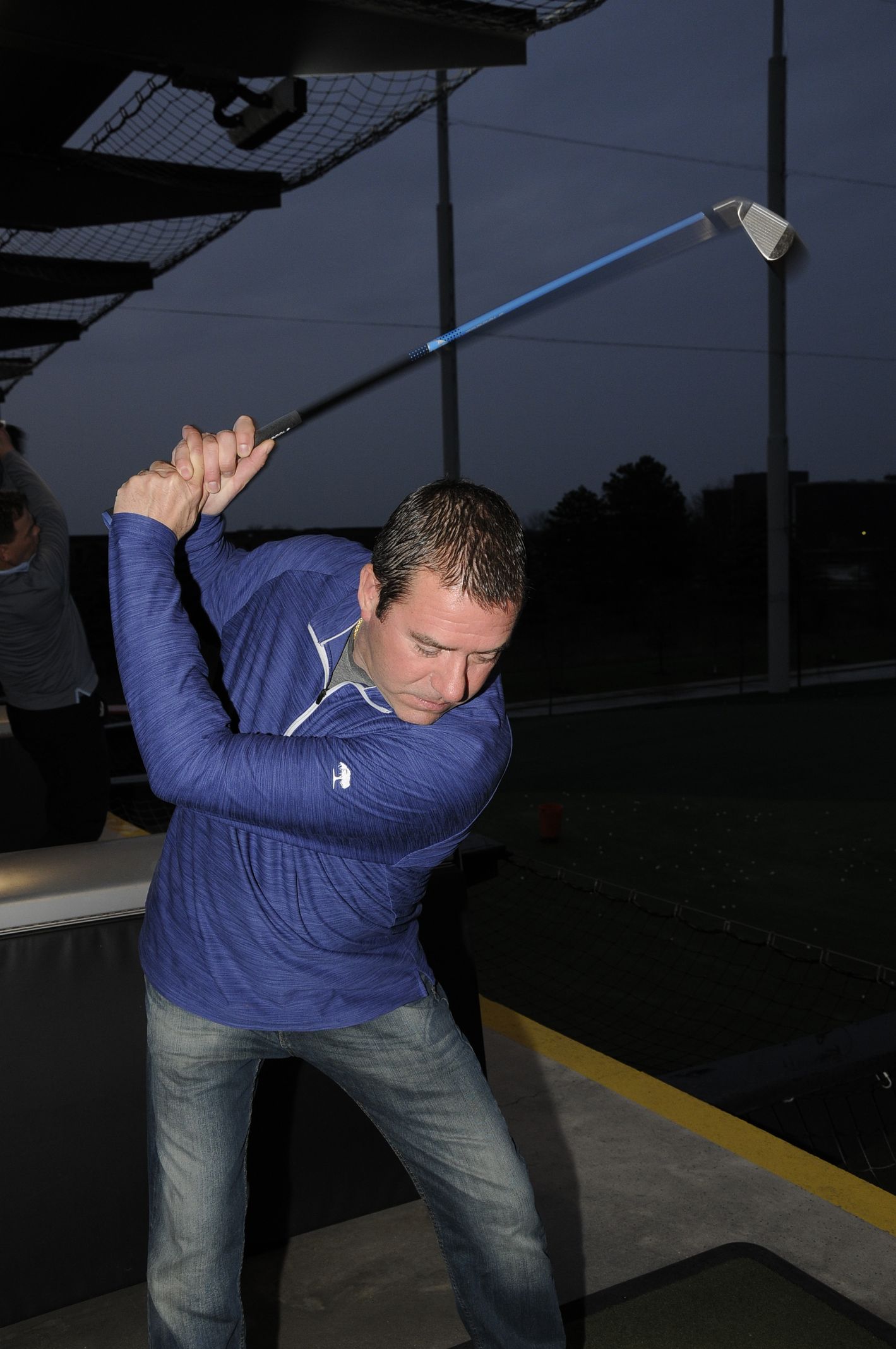 A man in a blue shirt is swinging a golf club