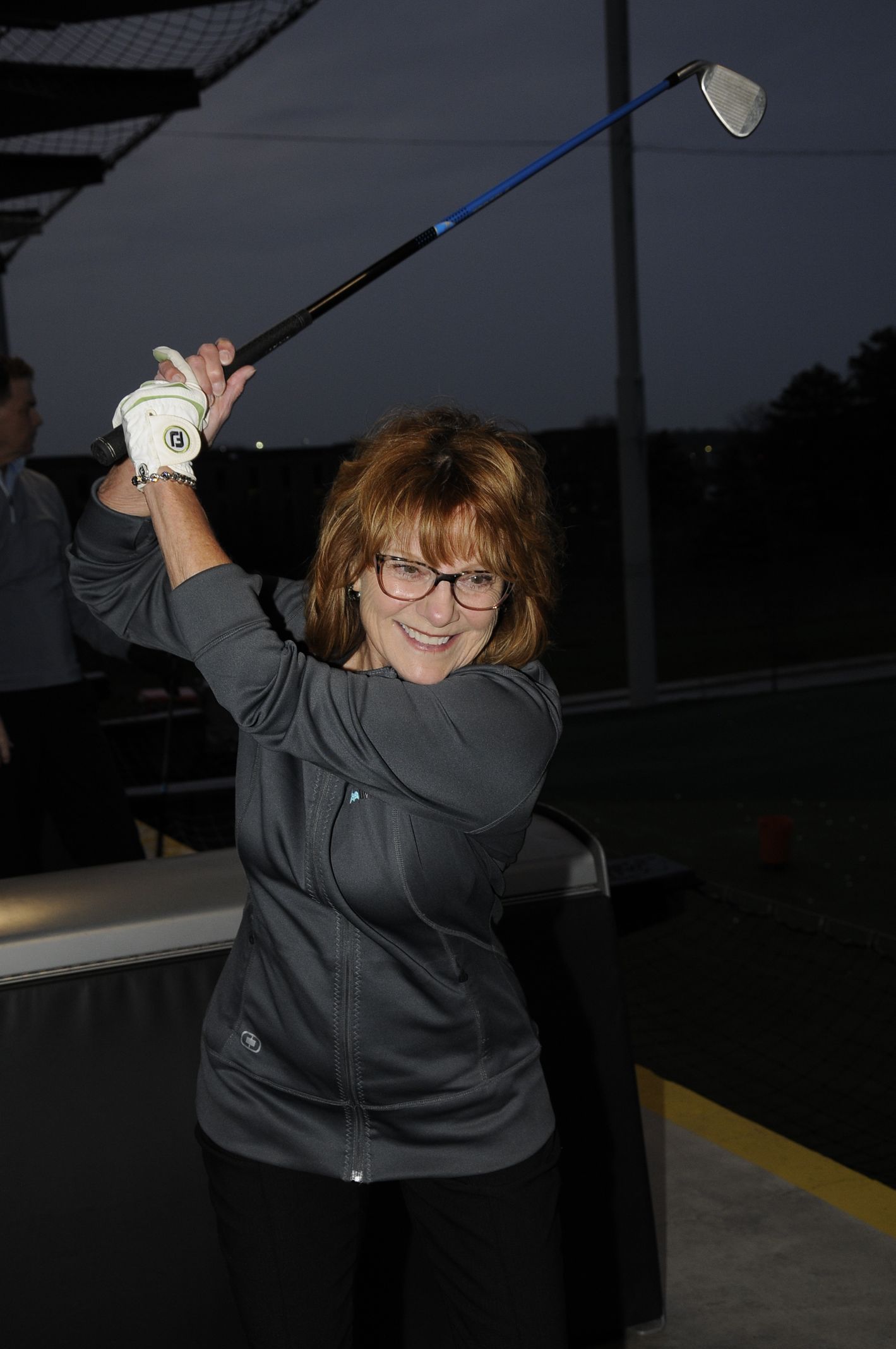 A woman wearing glasses is swinging a golf club