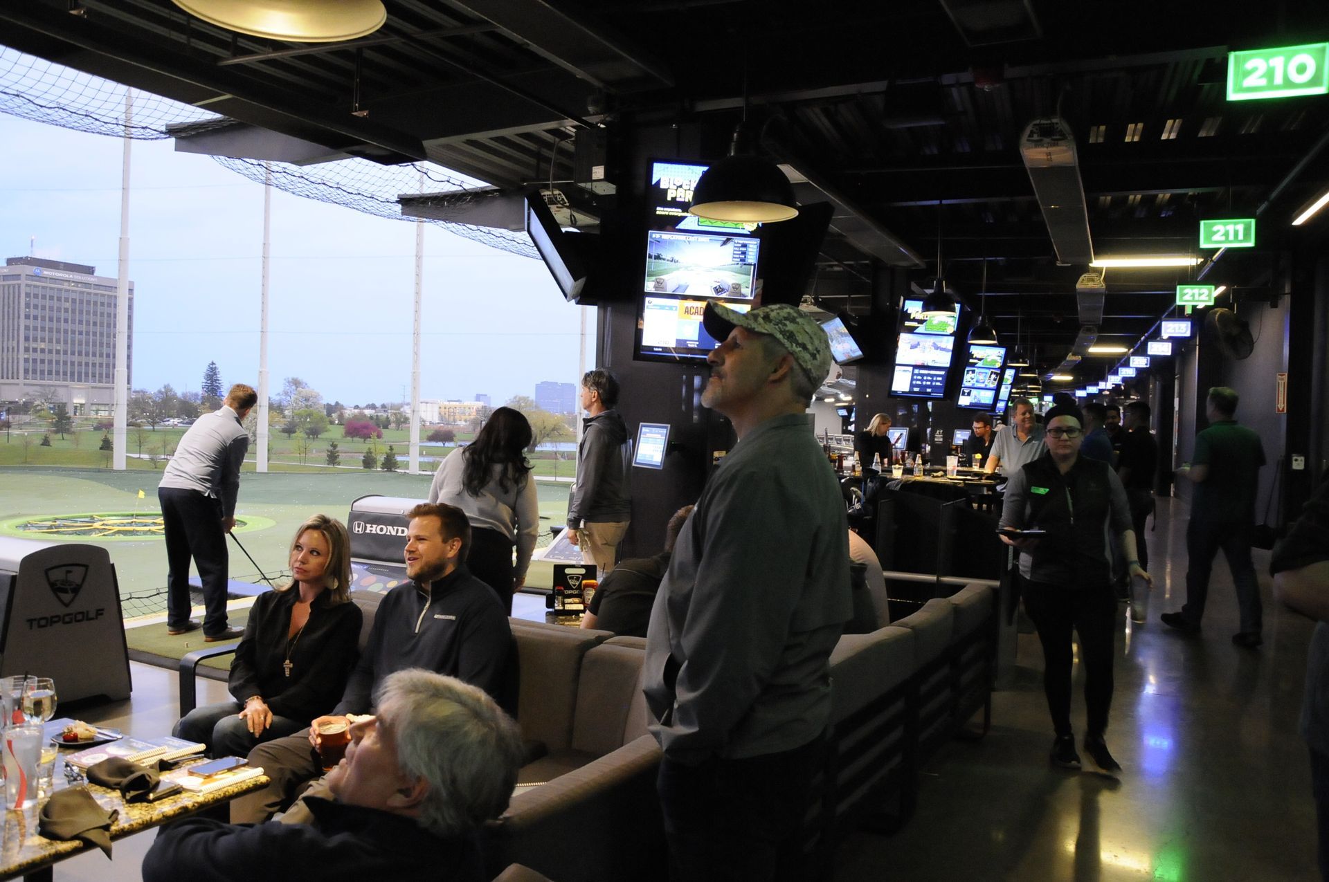 A group of people are sitting in a room with a sign that says 210