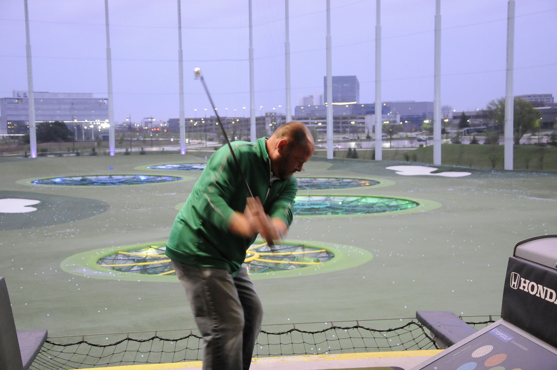 A man in a green shirt is swinging a golf club on a golf course.