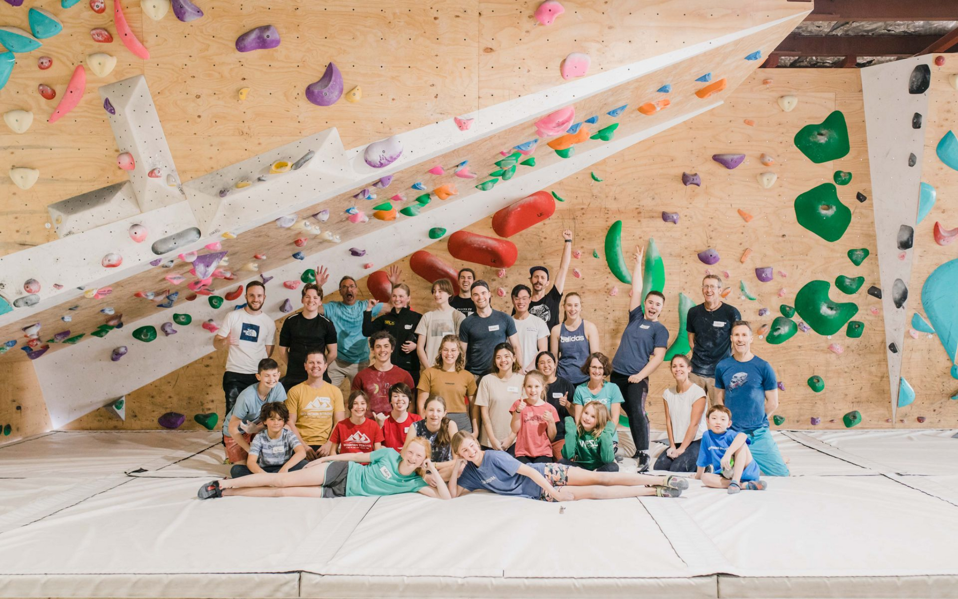 Large group of people pose in front of a climbing wall. 