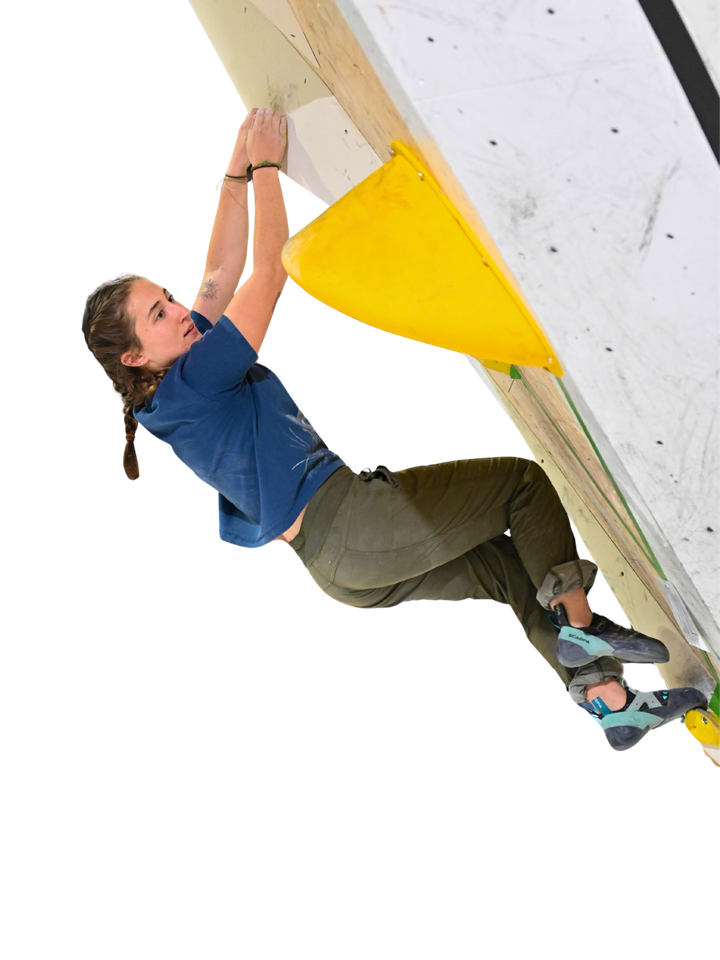 A climber in a blue shirt and green pants hangs from yellow and white climbing holds.