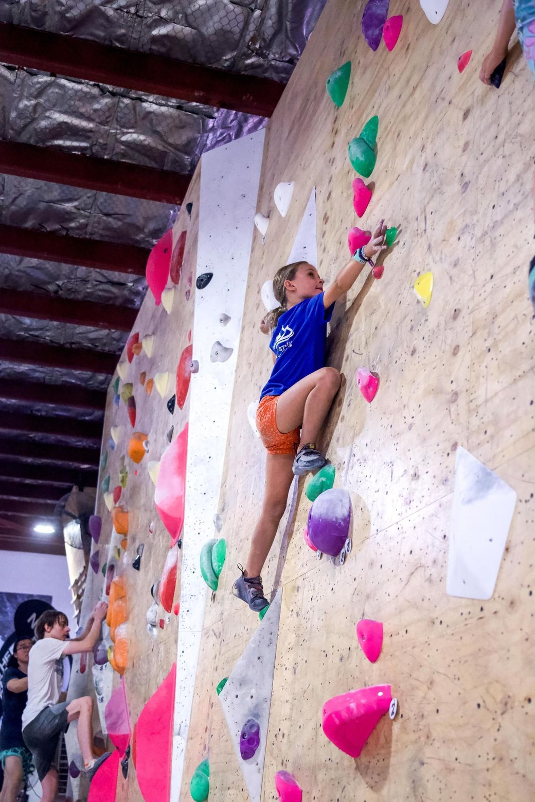 Girl climbing a colorful indoor rock wall, reaching for a hold.