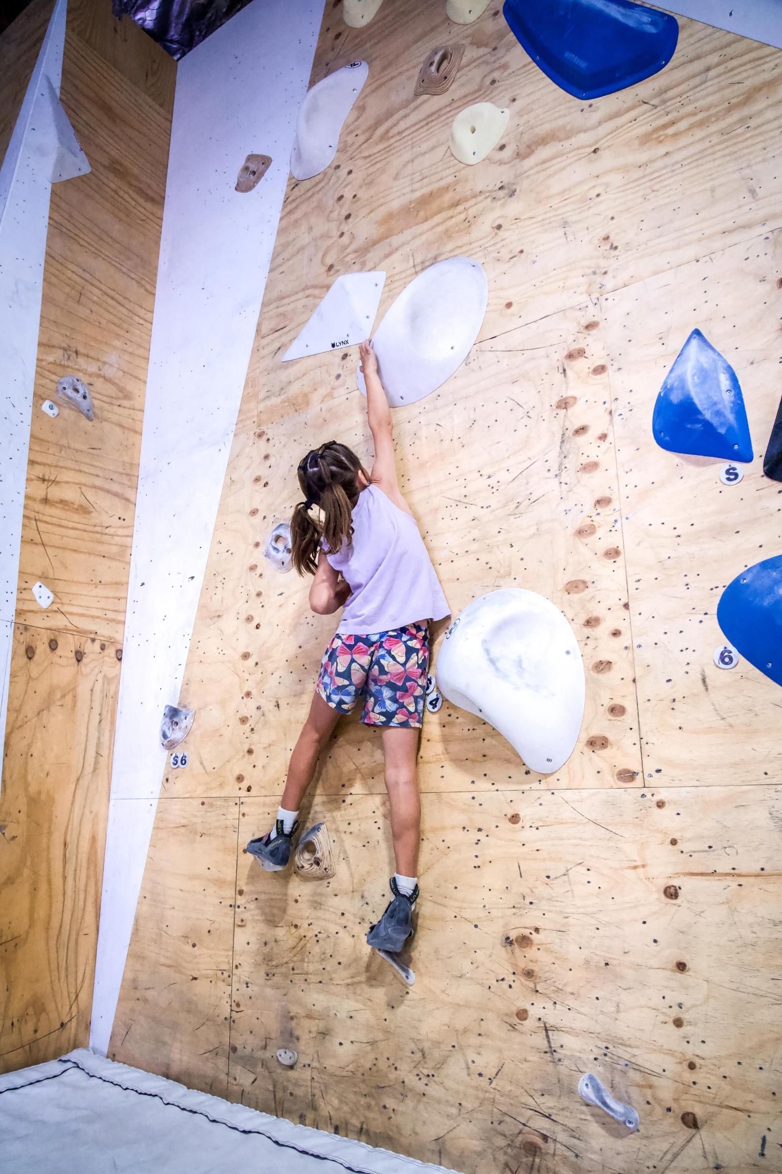 Person climbing a wooden climbing wall, reaching for a hold.