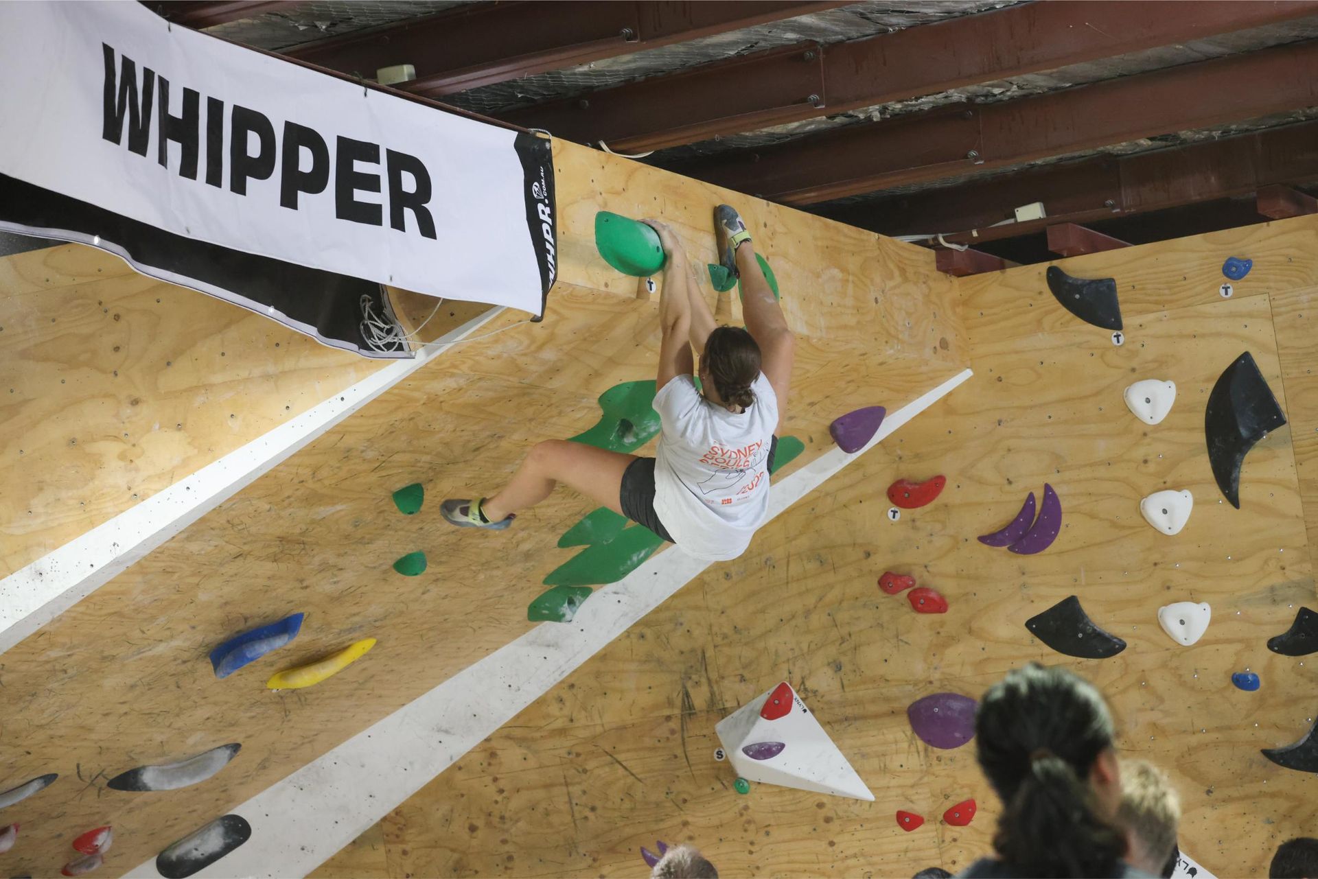 A climber grips holds on a slanted wall, reaching for the top. 