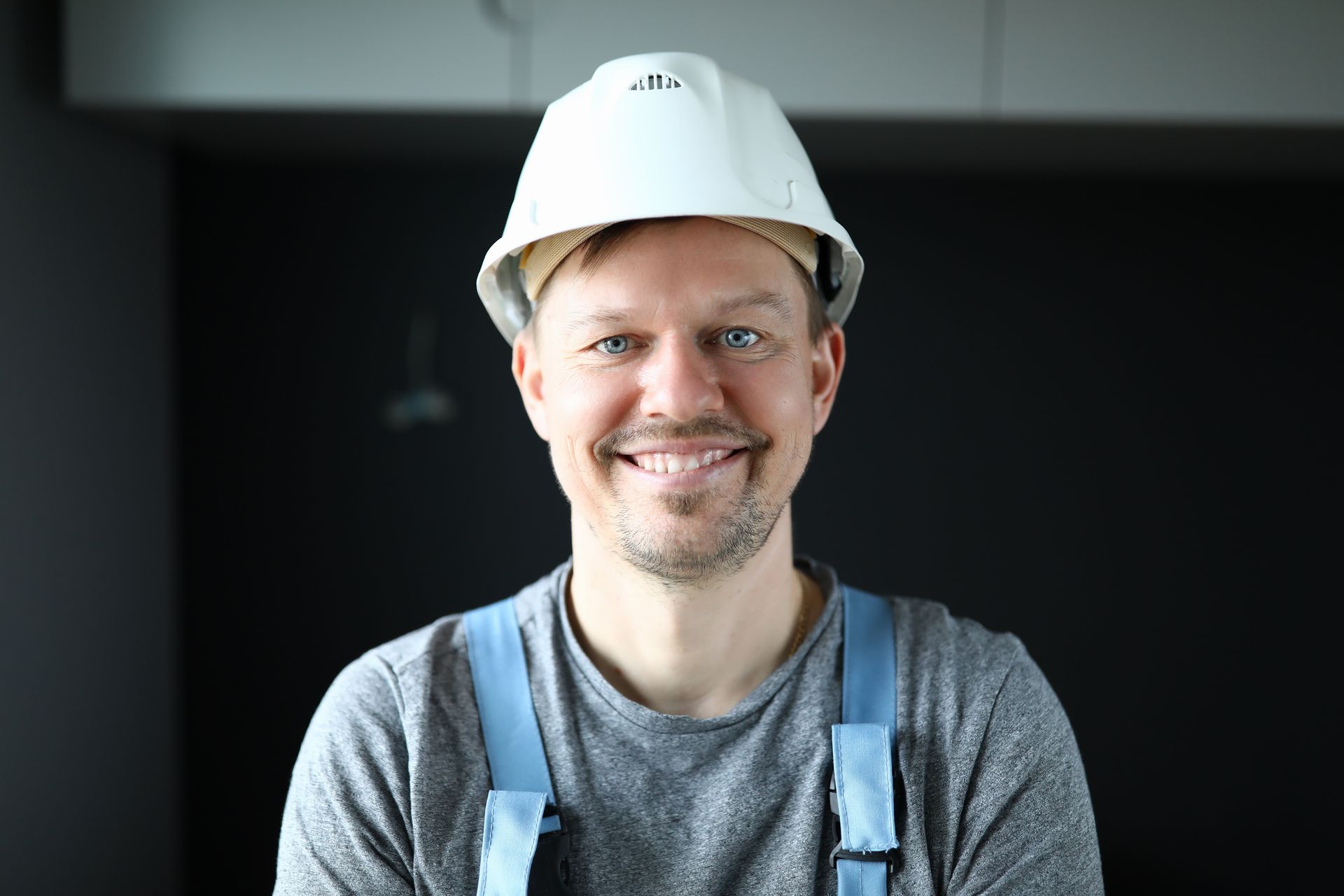 a man wearing a hard hat and overalls is smiling for the camera .