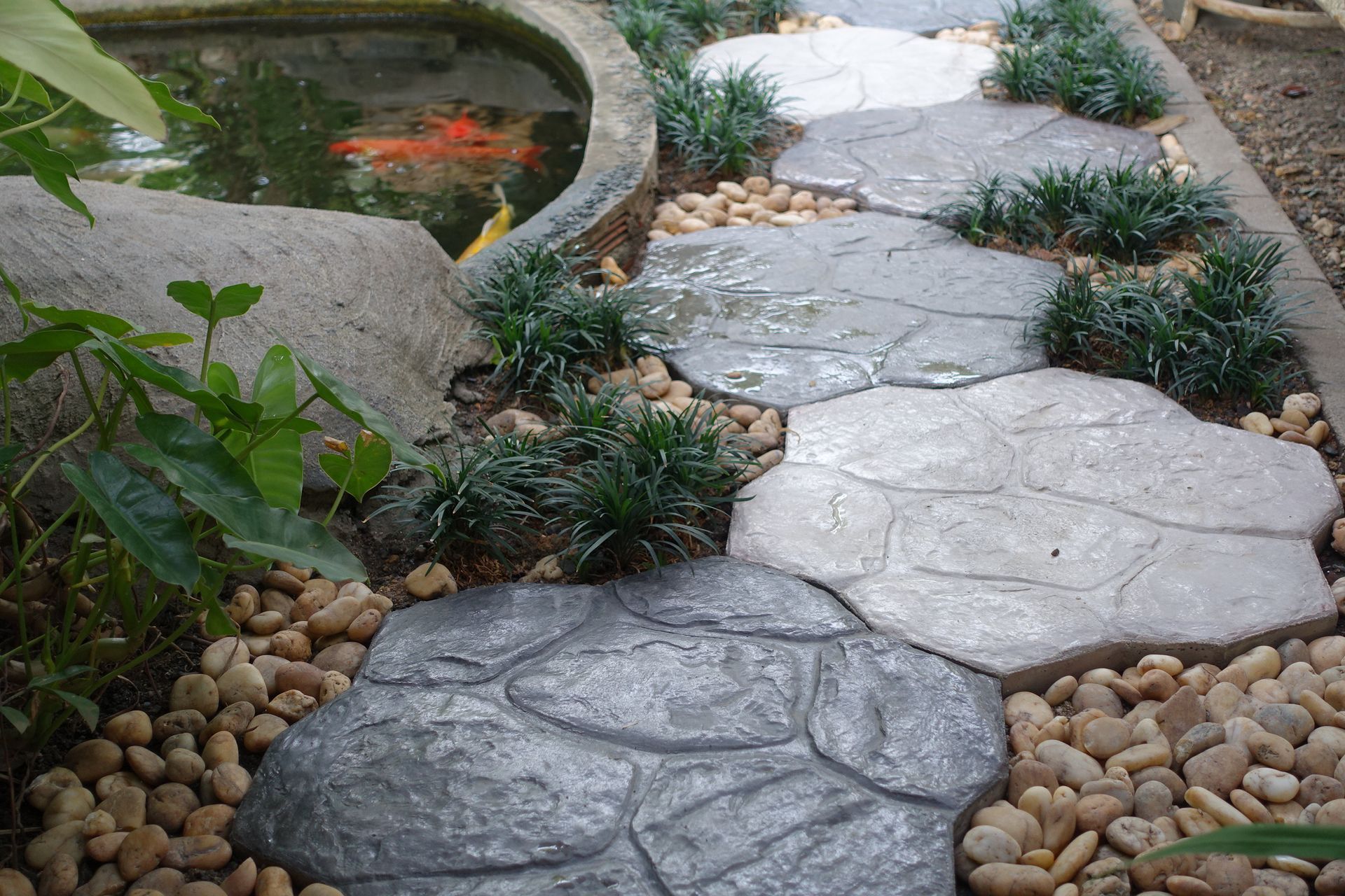 a stone walkway leading to a pond with fish in it