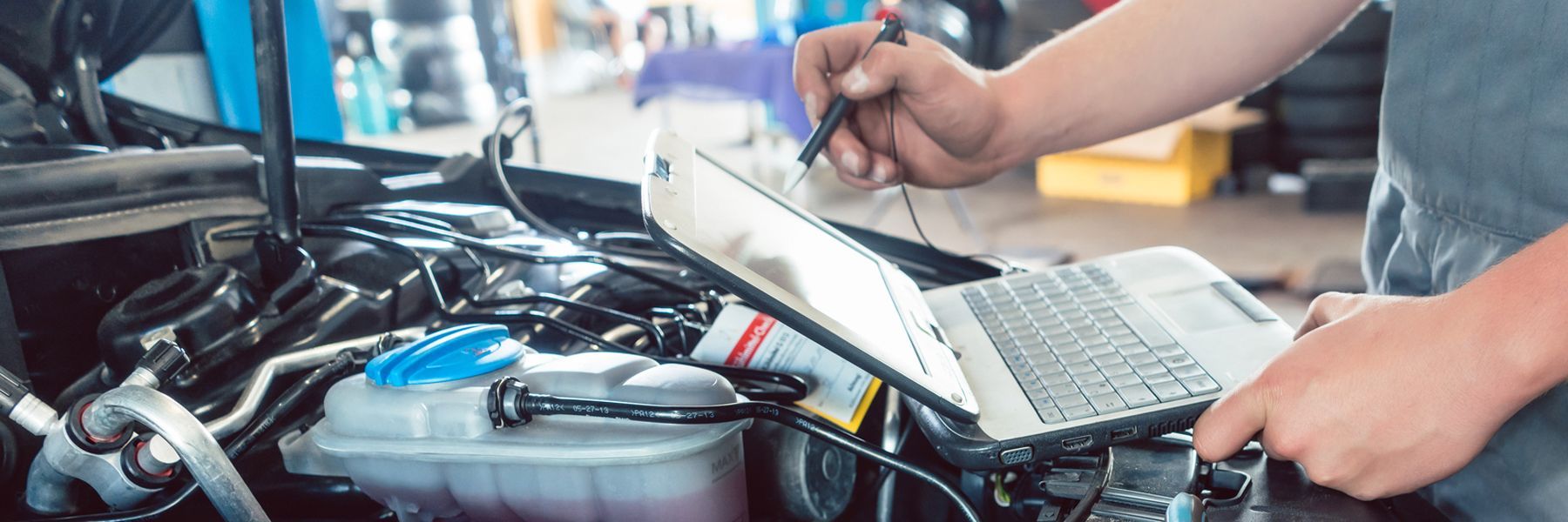 A man is working on a car engine while using a laptop computer.