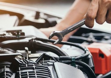 A person is working on a car engine with a wrench.