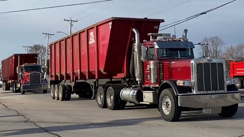 A trailer overflowing with scrap metal and debris parked on a street in front of a house.