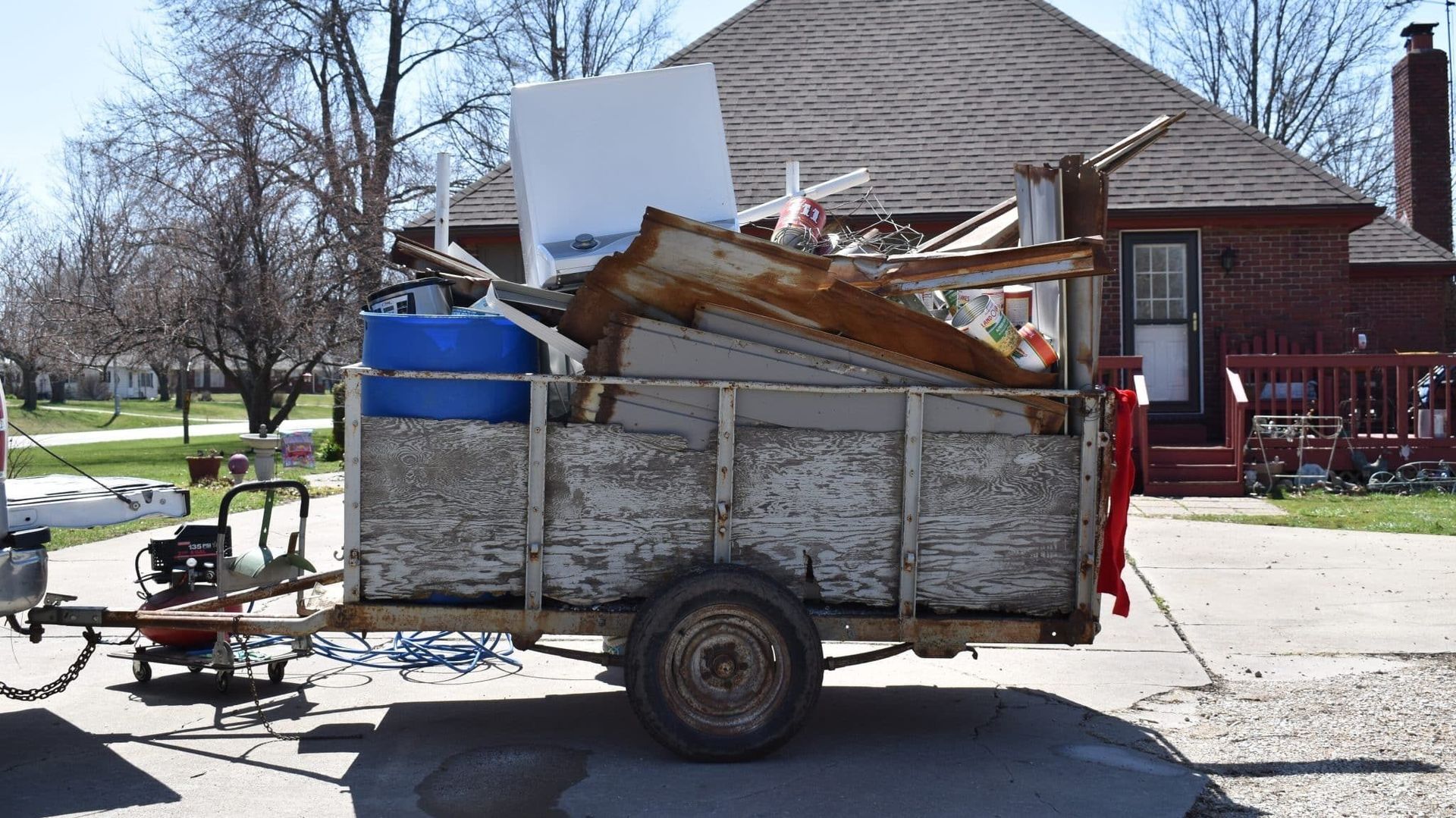 A trailer overflowing with scrap metal and debris parked on a street in front of a house.