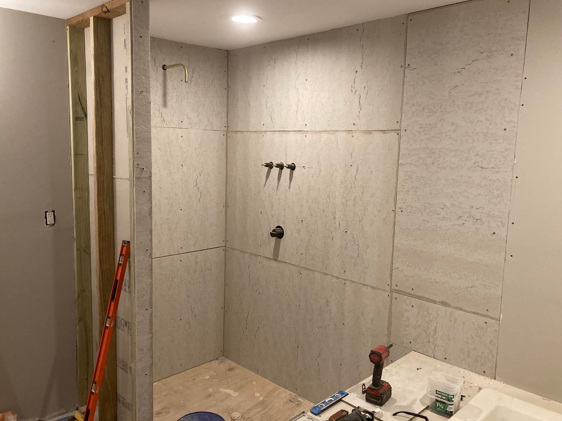 A shower under construction with cement board walls, plumbing fixtures installed.