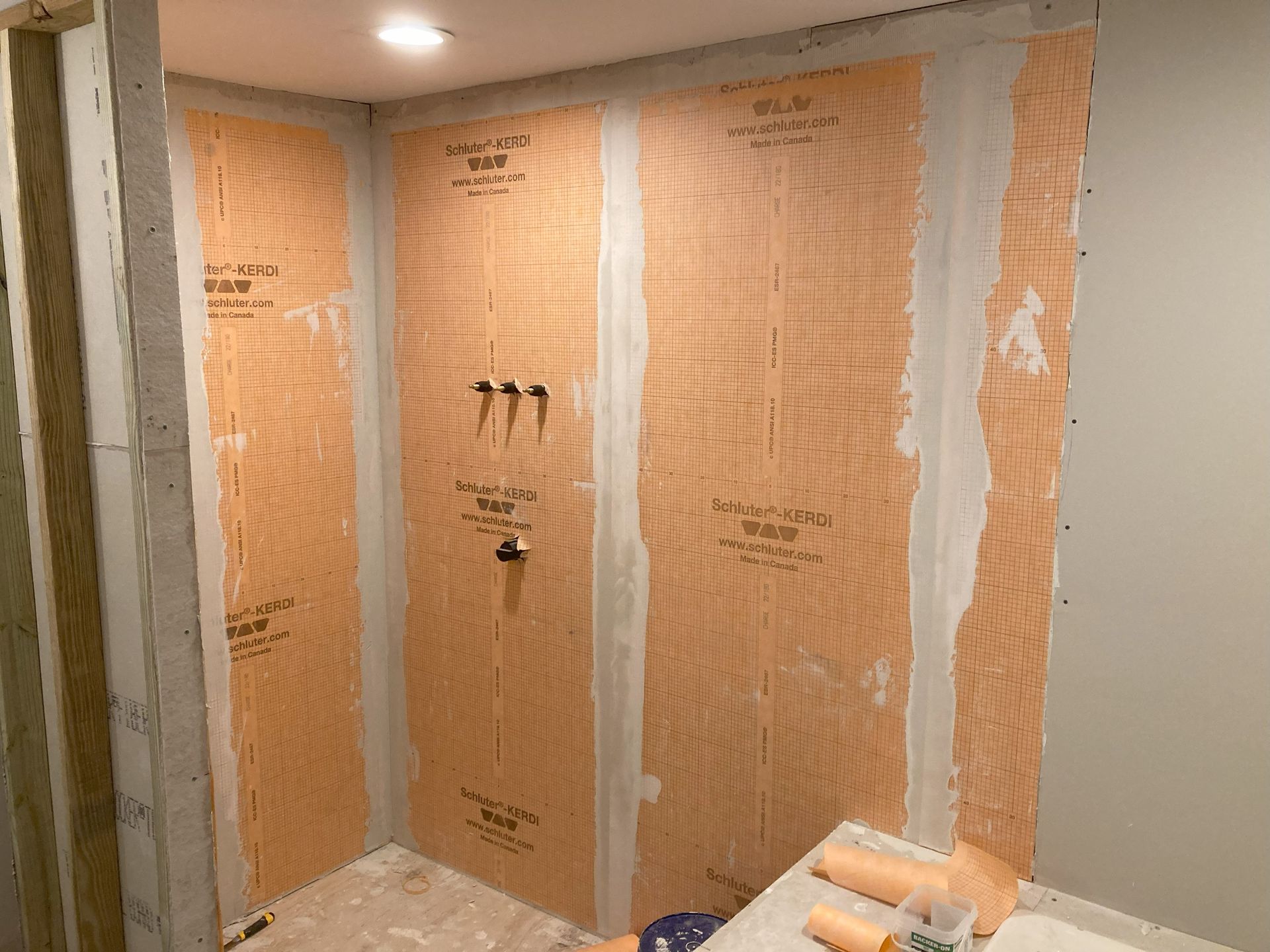 Shower stall under construction, orange waterproof panels installed on the walls, with plumbing fixtures visible.