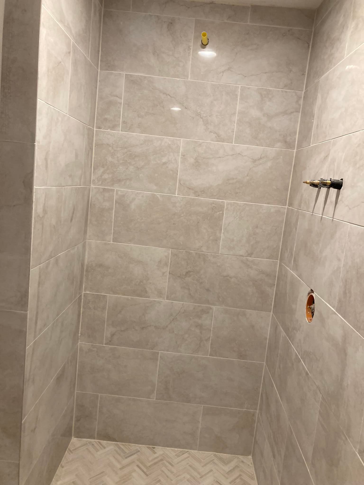 Tiled shower stall with gray walls, fixtures, and a herringbone floor.
