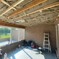 Ceiling renovation with exposed beams and insulation, brick wall, ladder, and tools.