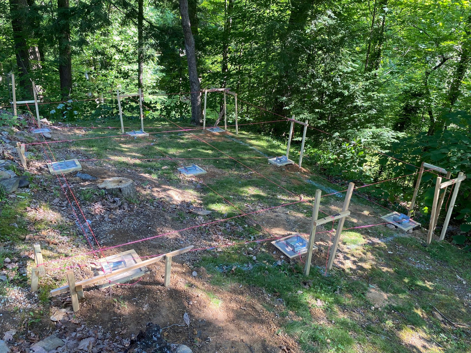 A construction site in a forest with wooden frames and concrete squares on the ground.