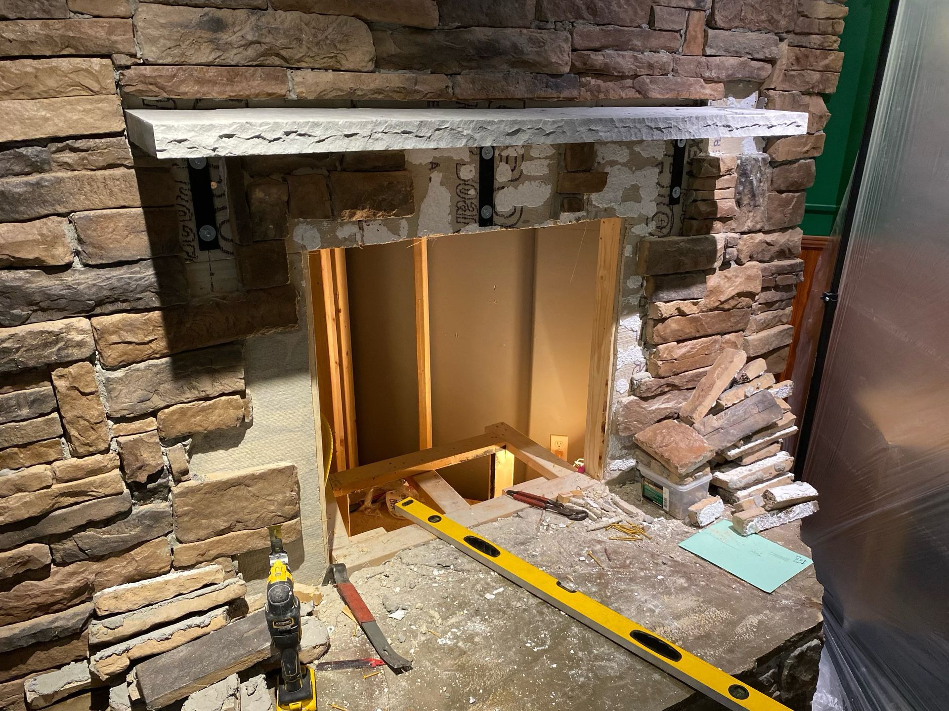Fireplace under construction: stone facade, exposed framing, level, and shelf in place.