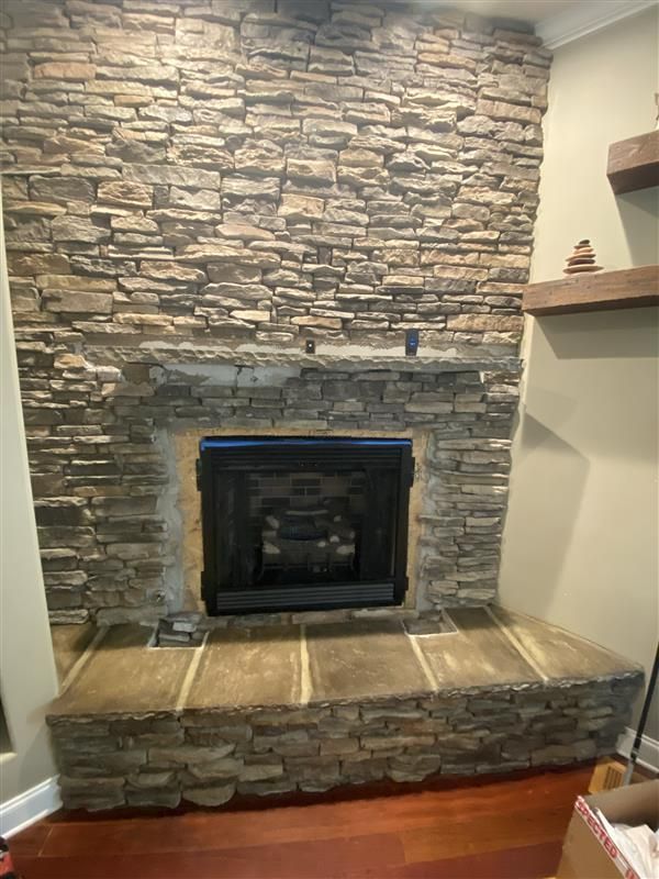 Stone fireplace with a black firebox, light-brown stone hearth and surround, built-in to a stone wall.