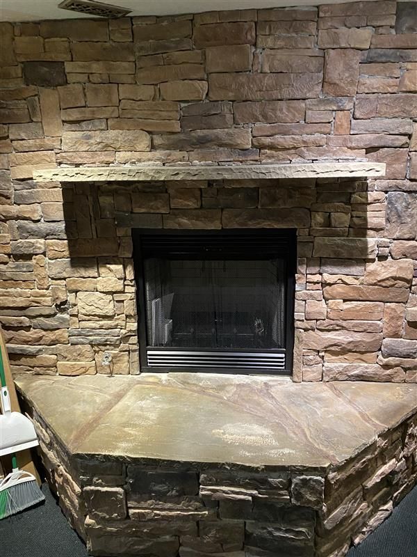 Fireplace with stone surround and hearth. Stone mantel above the black fireplace.