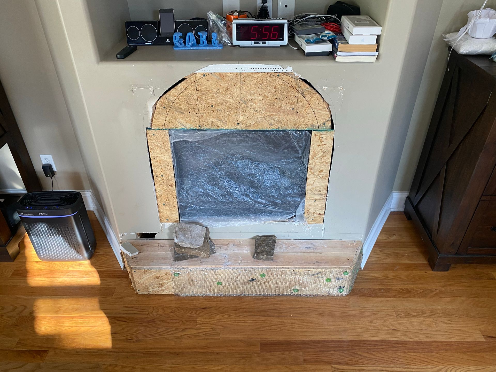Fireplace niche with exposed inner structure and unfinished wood surround, with electronics on a shelf above.