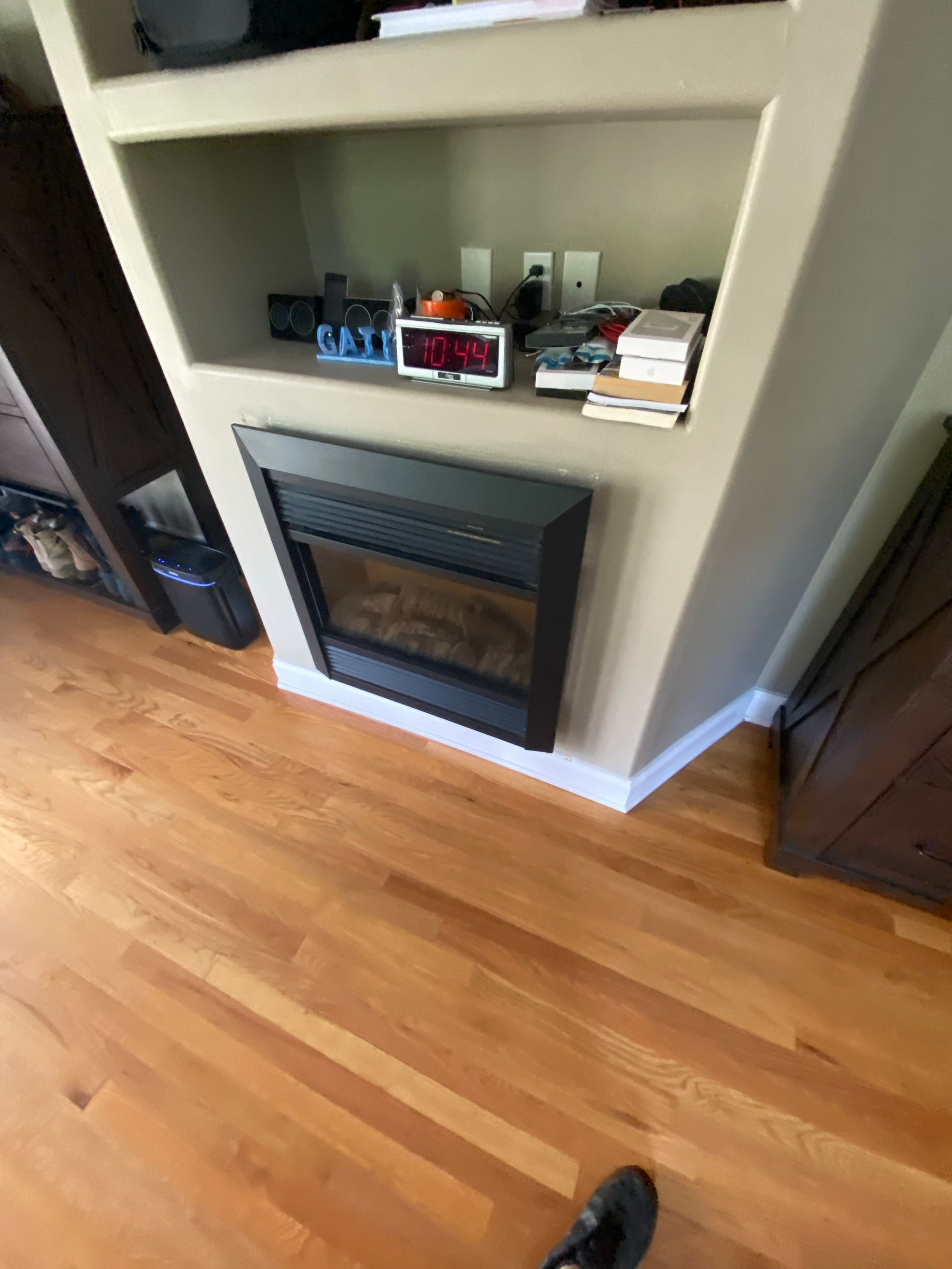 Built-in fireplace with a shelf above, set in a beige alcove. Light wood floor, dark fireplace and a few objects on the shelf.