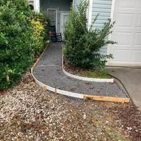 Gravel pathway curves past bushes, with a door and building in the background.