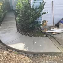 Curving concrete sidewalk leading to a house, with a bush on the left side.