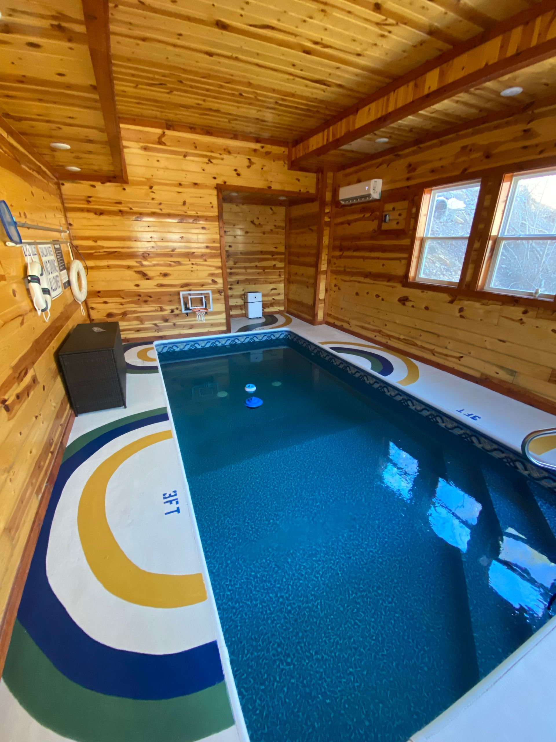 Indoor pool with blue water, surrounded by wood paneling and a colorful painted floor.