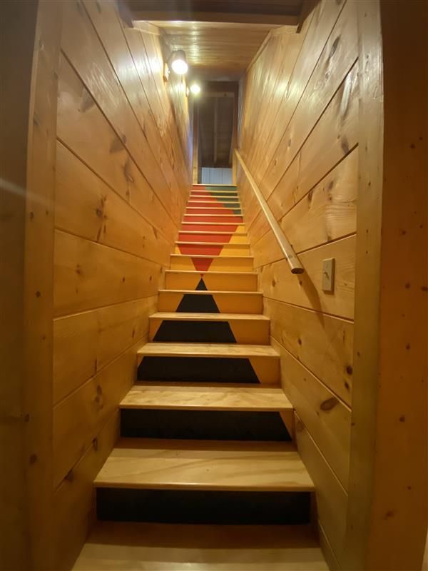 Wooden staircase with painted geometric shapes on the risers, wood-paneled walls, and a handrail.