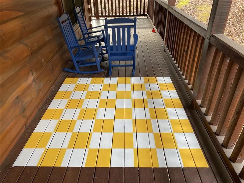 Wooden porch with checkerboard flooring, blue rocking chairs, and a log cabin wall.
