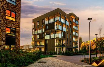 Modern apartment building with balconies, brick facade, and warm sunset lighting.