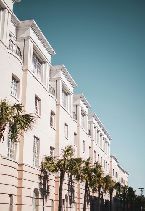 Beige building with white accents, palm trees, and a bright blue sky.