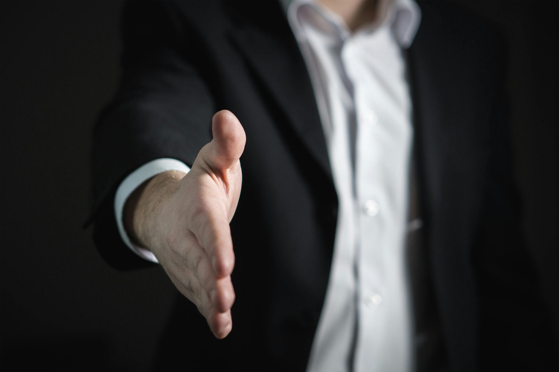 Person in a suit extending hand for a handshake.