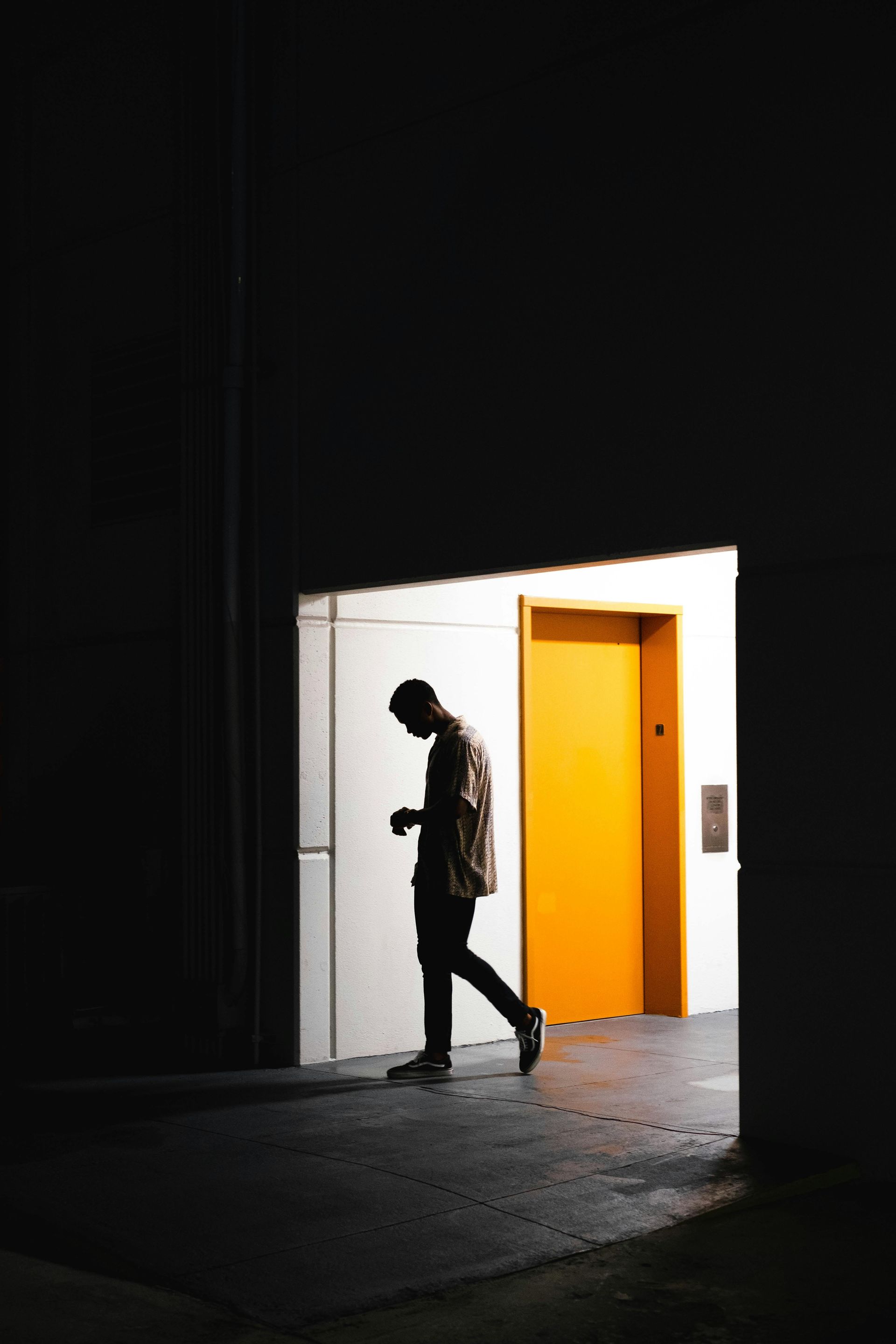 Silhouette of a person walking toward a bright doorway with an orange door. Dark setting.