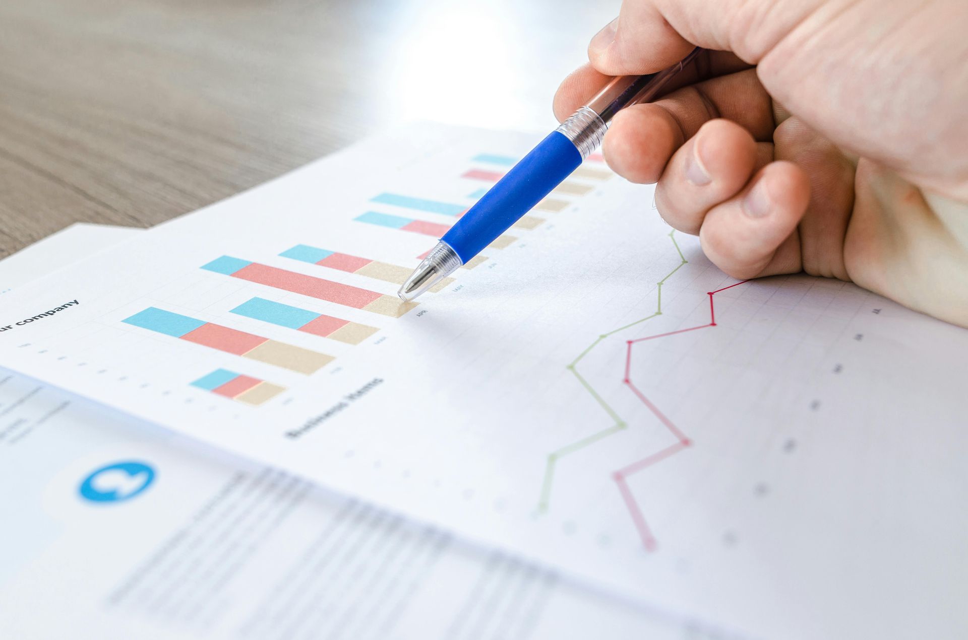 Hand holding blue pen pointing at business charts.