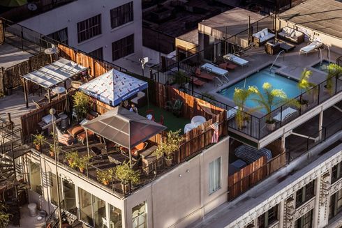 Rooftop pool and lounge area with umbrellas, seating, and a surrounding fence on top of a building.