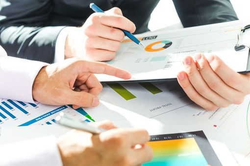 Hands pointing at and holding financial charts and data.