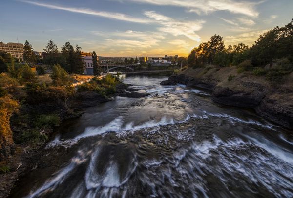 A river with a waterfall in the middle of it at sunset.