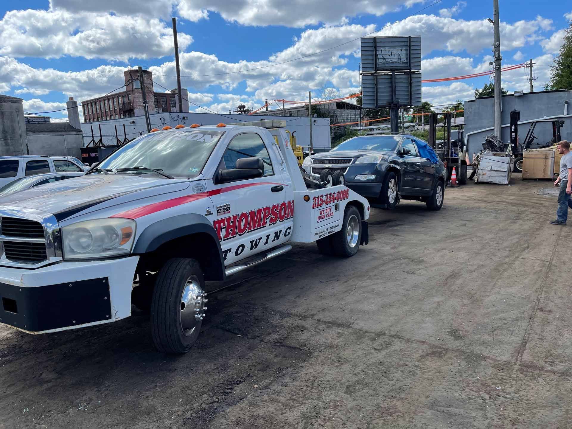 A Thompson towing truck is towing a car in a parking lot.