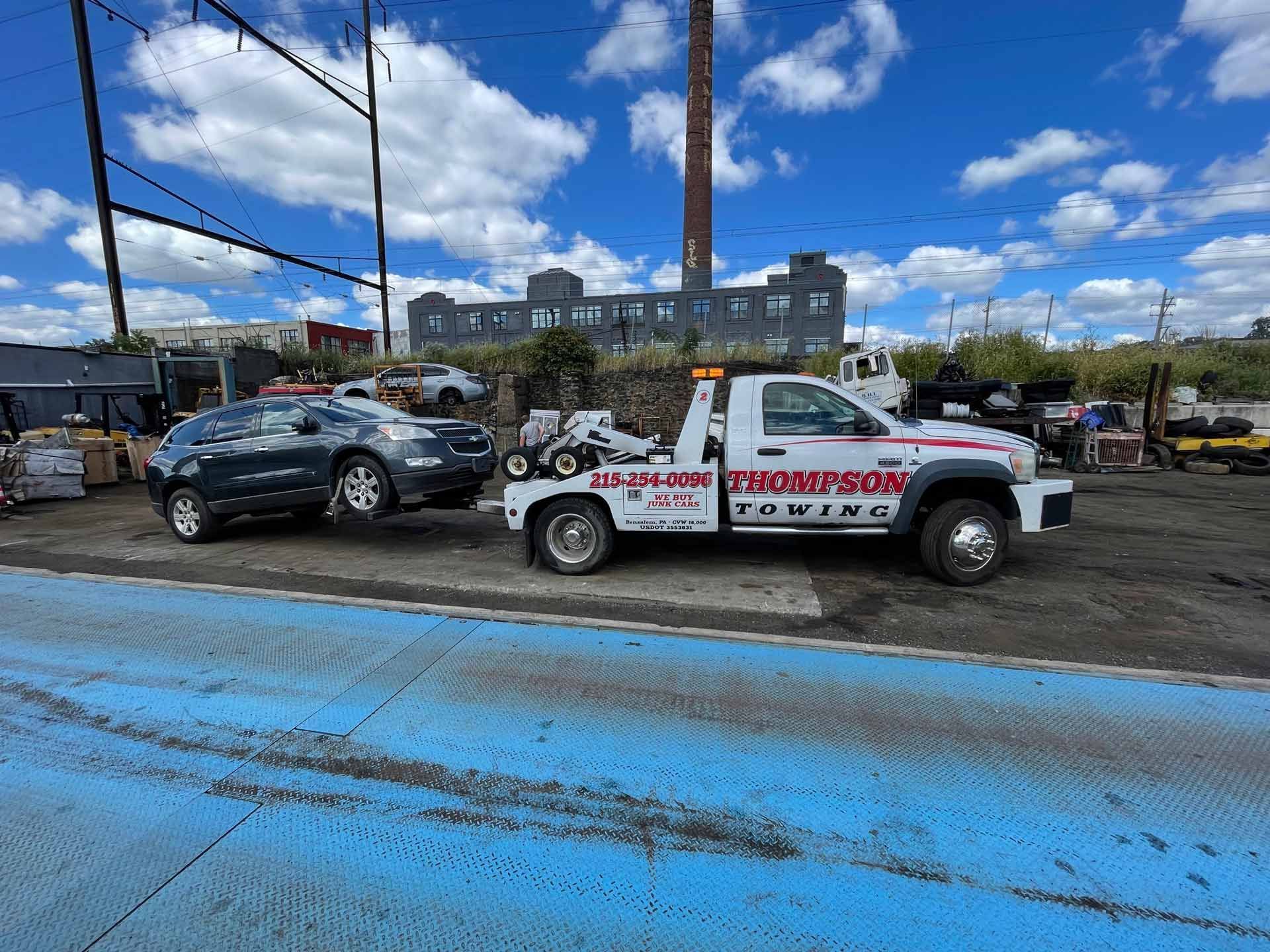 A photo of Thompson towing truck towing a junk car on the street