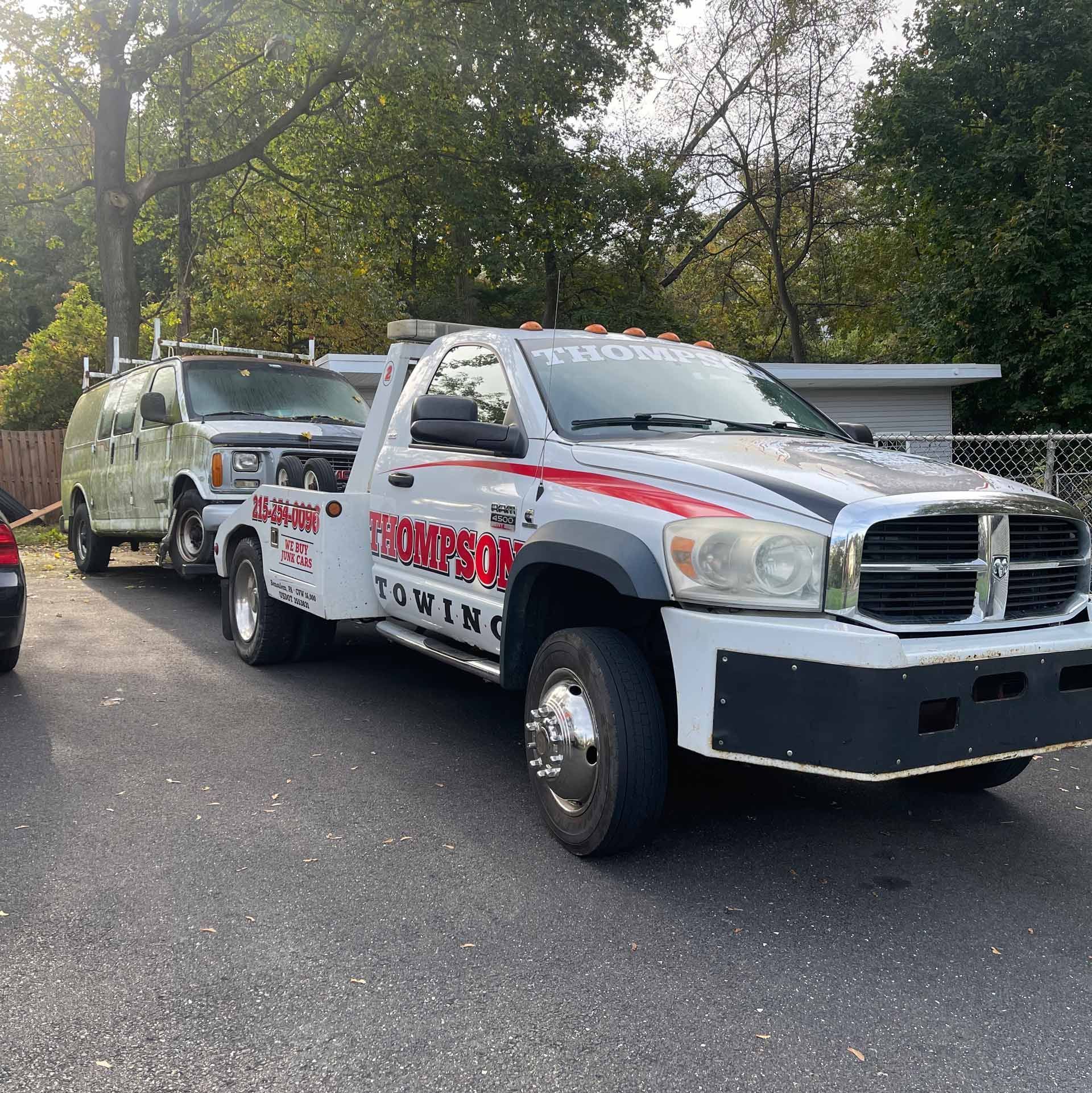 A Thompson Towing truck is towing a junk car