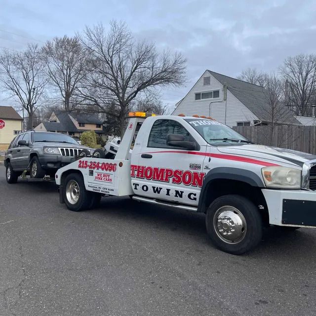 A tow truck from Thompson Towing tows a gray SUV on a street of Parkland, PA.
